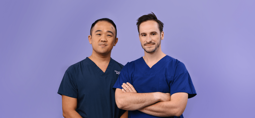 Two members, dressed in medical scrubs, stand in front of a purple background.