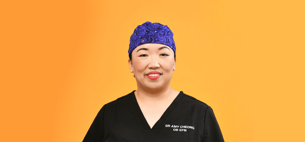 Dr Amy Cheong wearing scrubs smiles at camera against yellow background