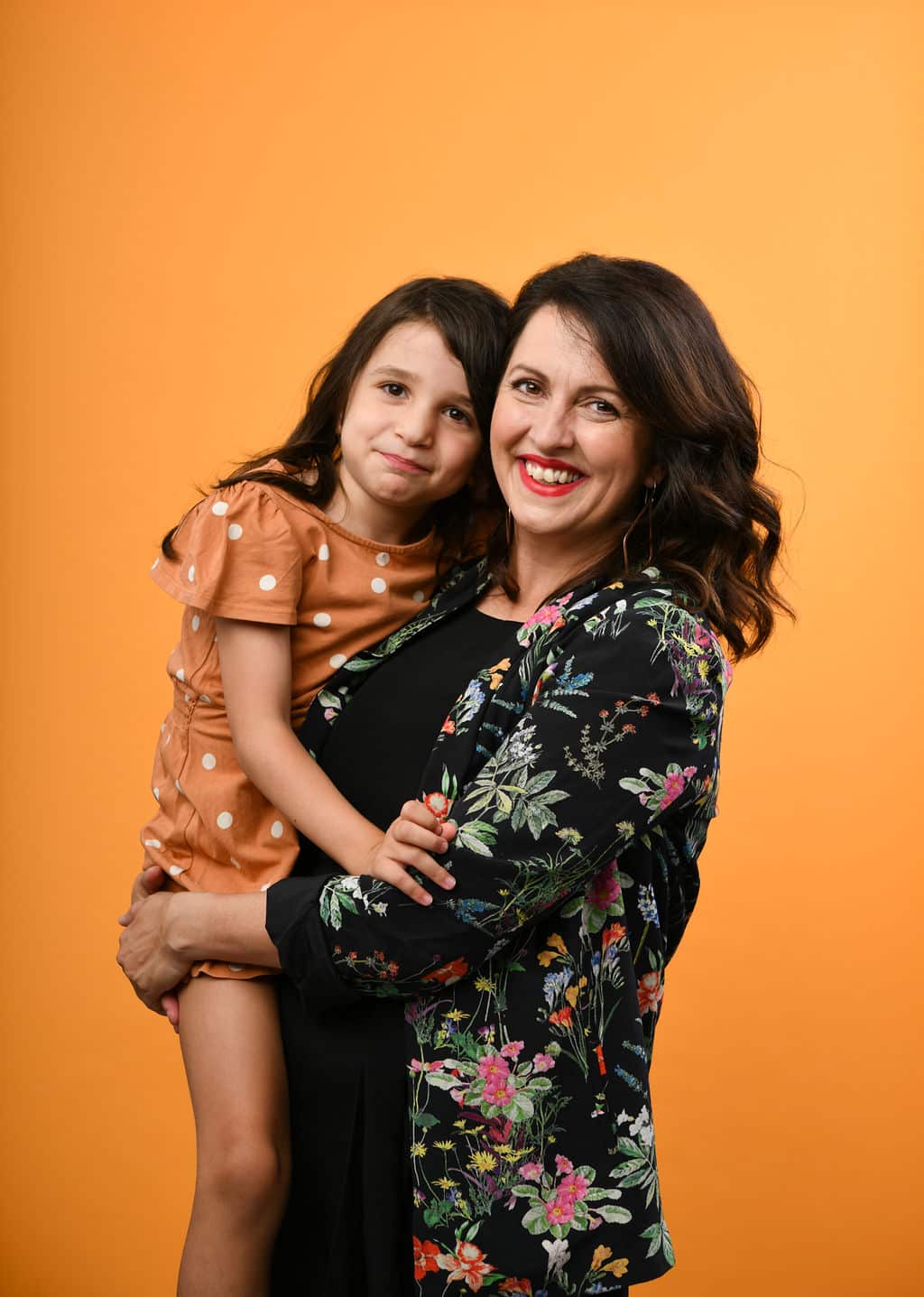 A mother holding her daughter against a yellow background