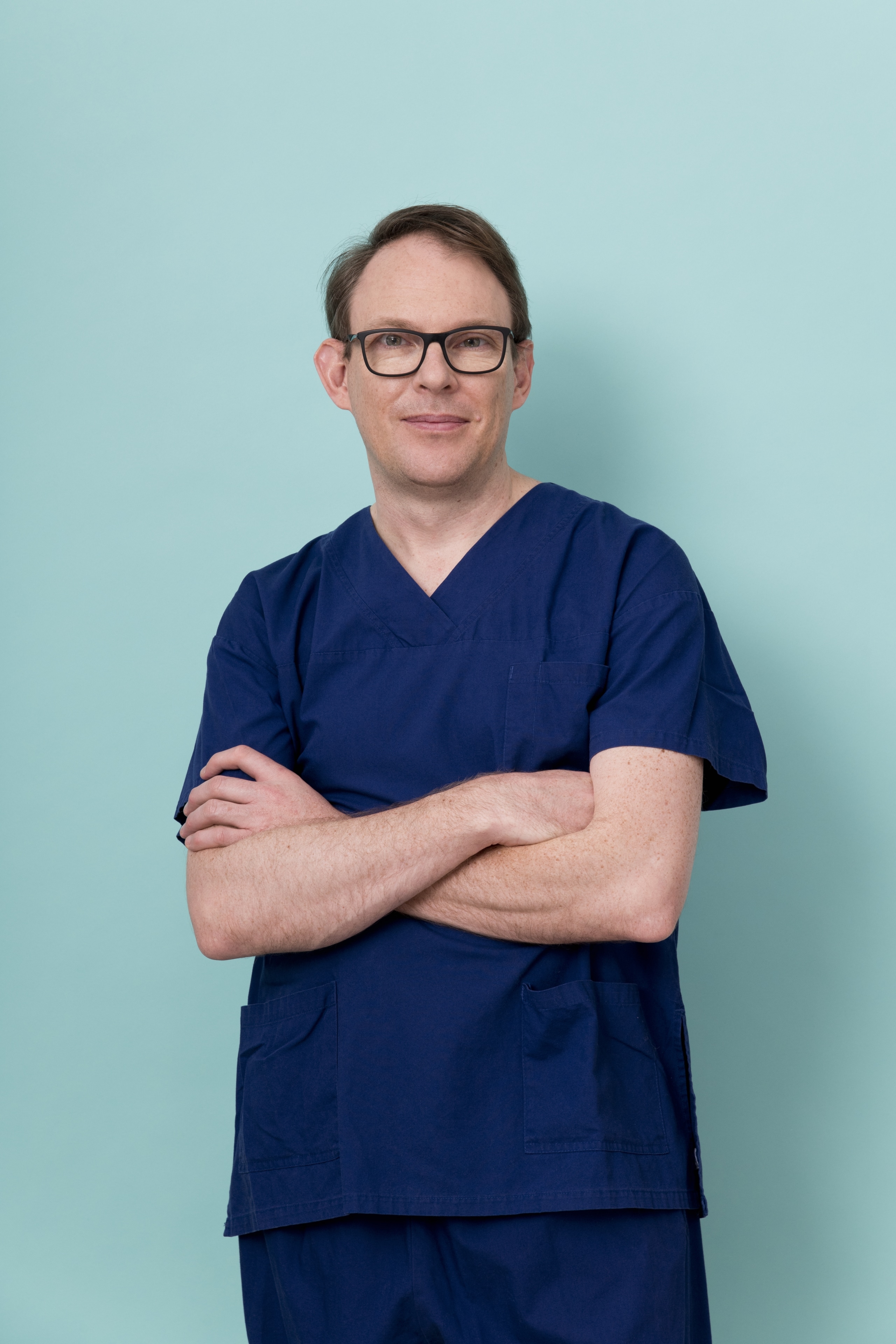 Portrait of male obstetrician wearing scrubs against a teal background