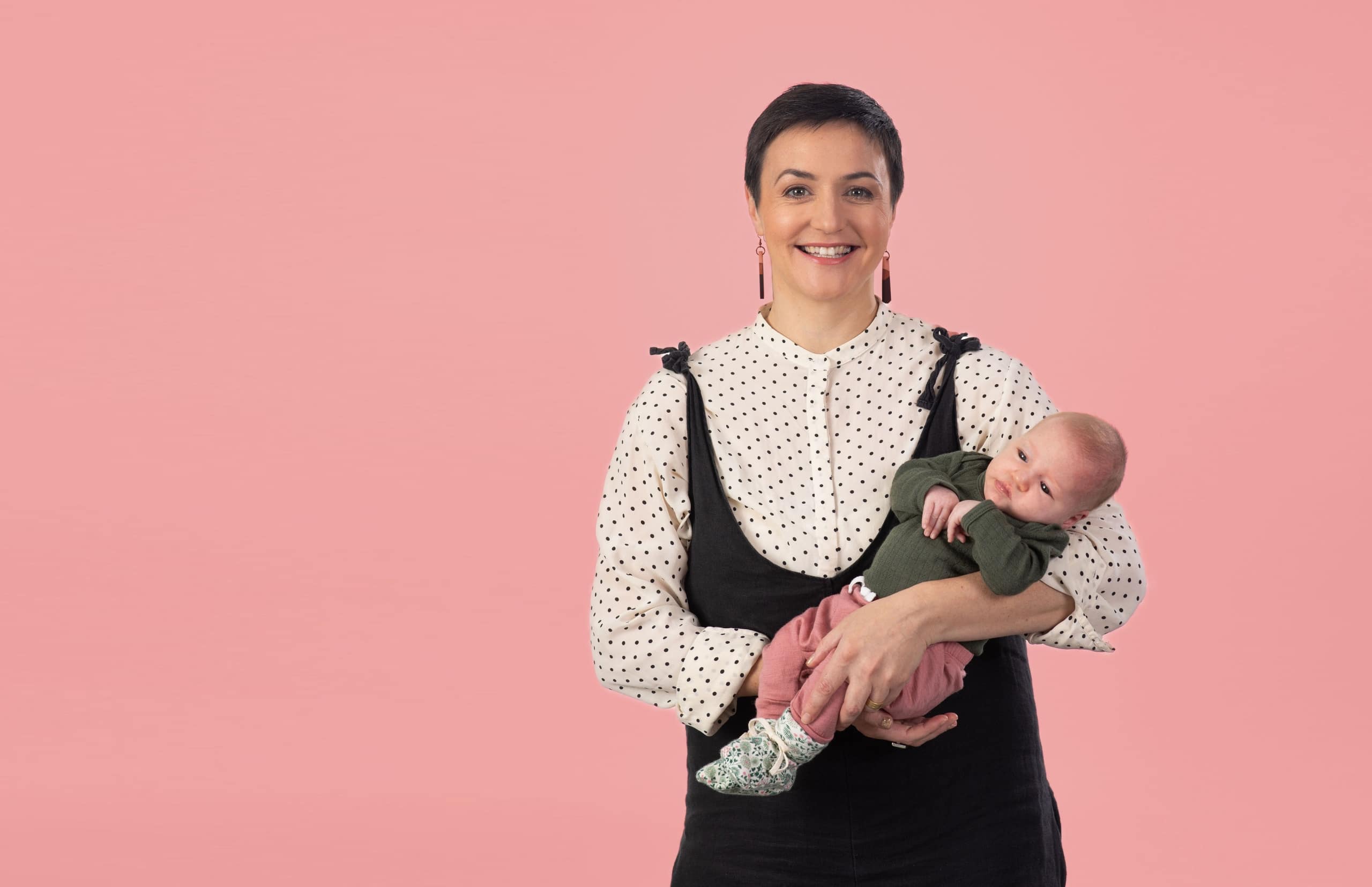 Portrait of Māori Fellow Dr Sarah Te Whaiti and her baby daughter against a pink background.